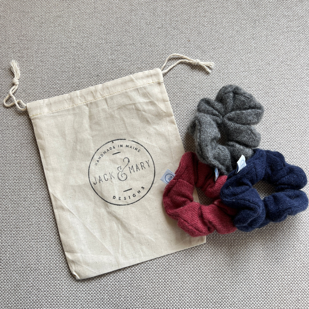 A set of 3 cashmere scrunchies with a logo muslin drawstring bag