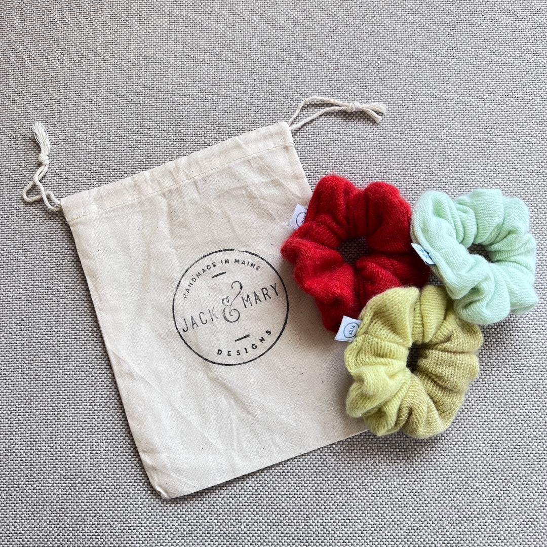 A set of 3 cashmere scrunchies with a logo muslin drawstring bag